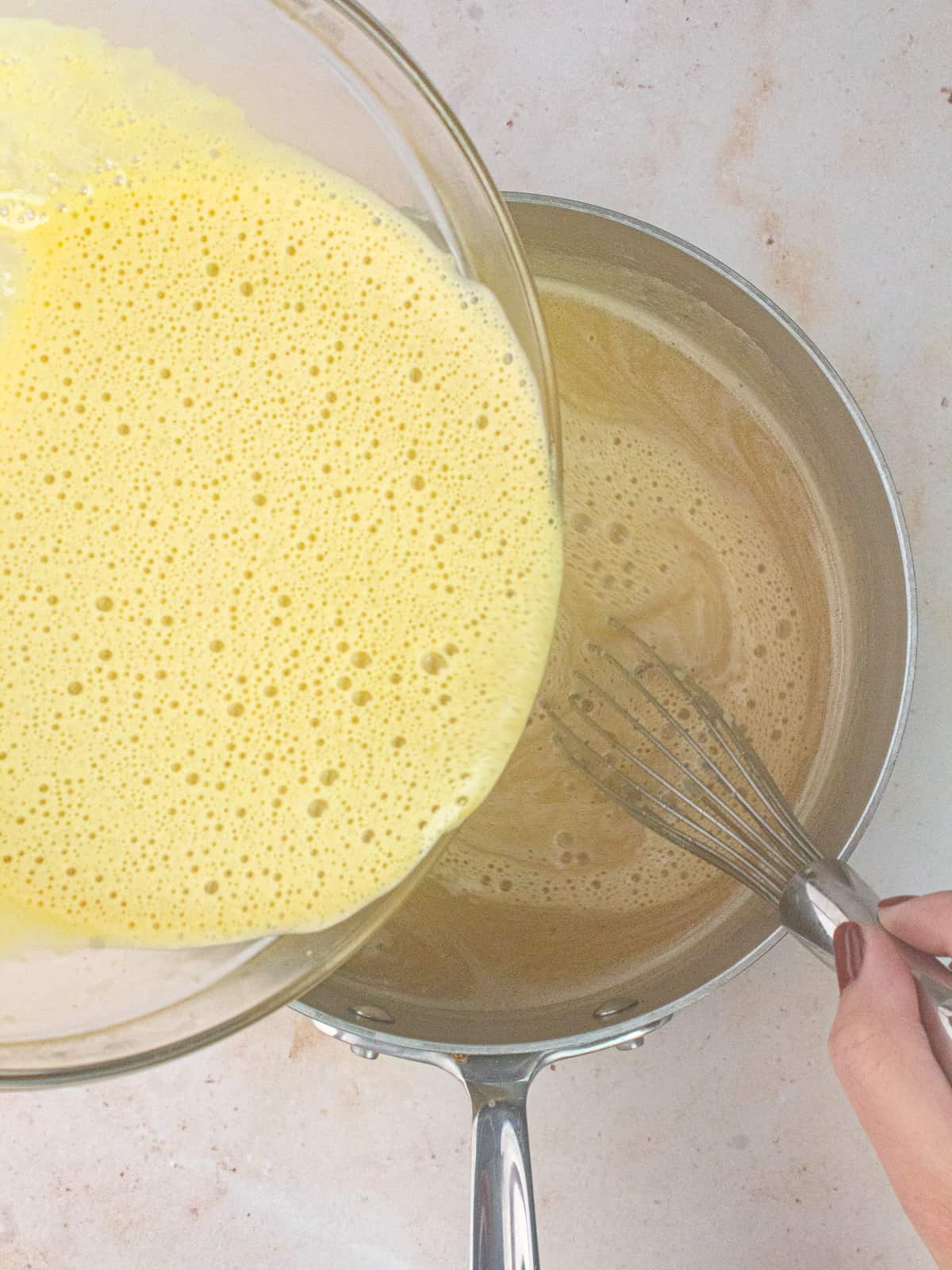 pouring tempered yolks into saucepan of cream