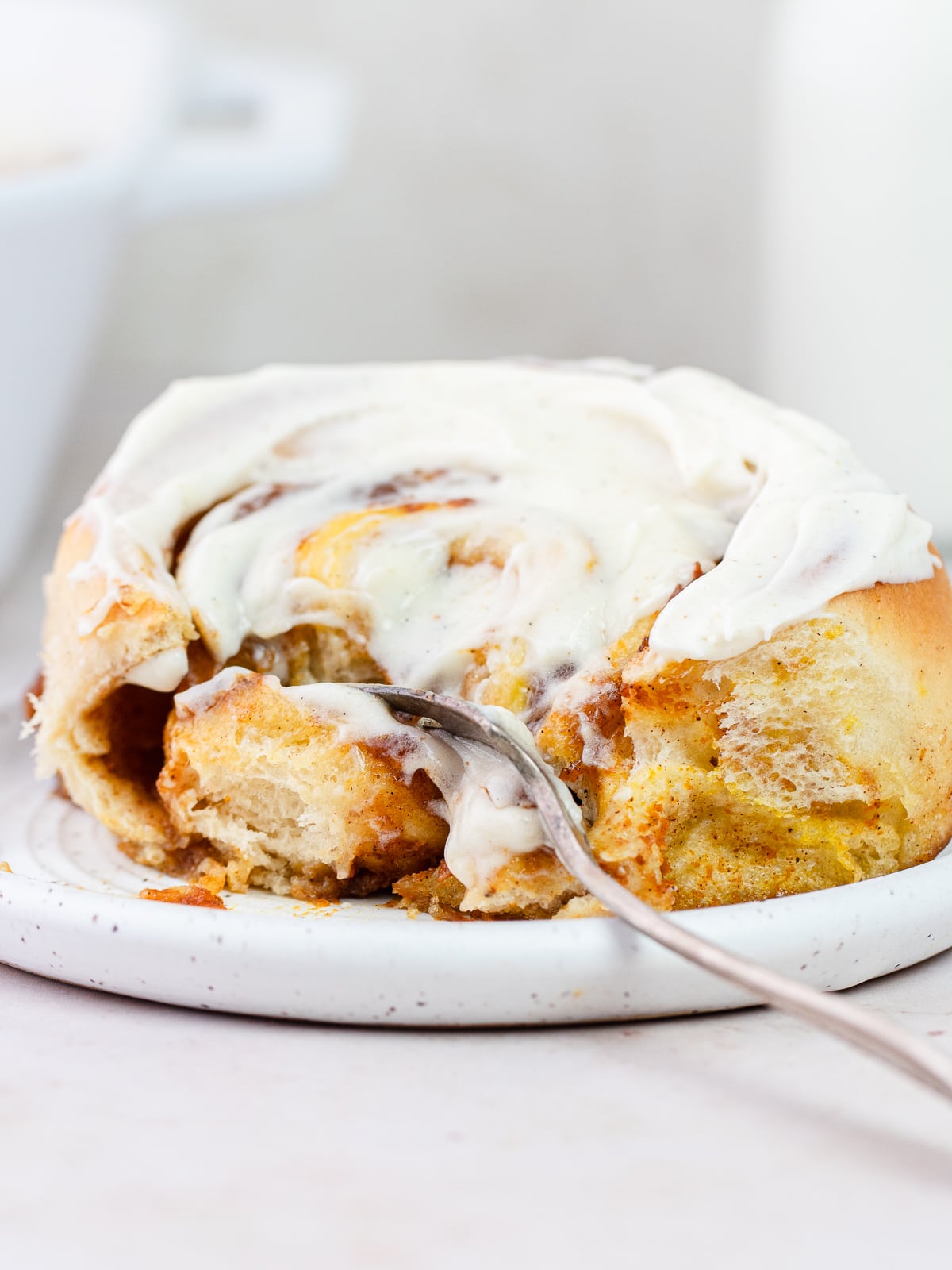 Close up of a cinnamon roll on a plate with a fork through it