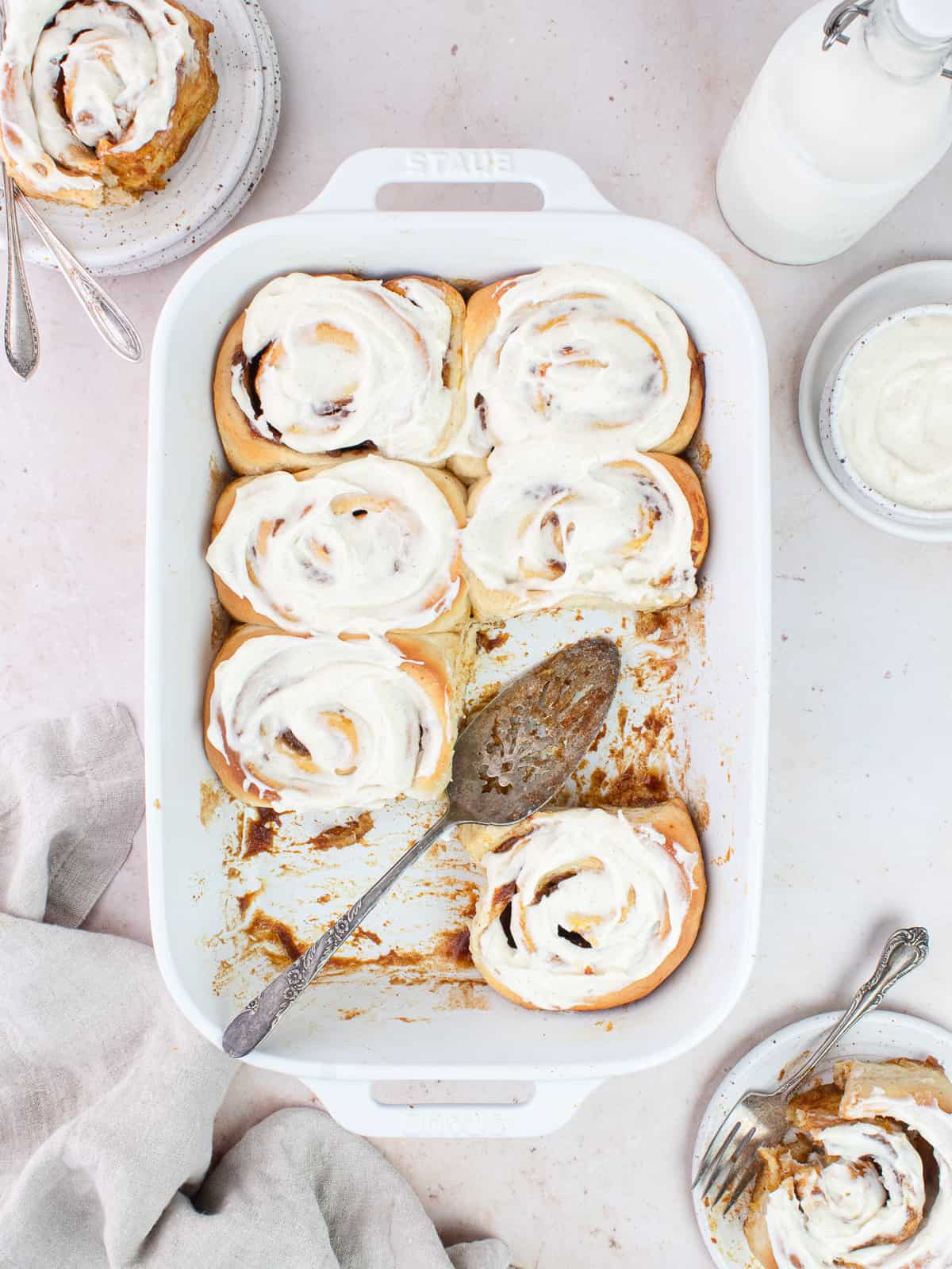 Tray of cinnamon rolls and plates and milk jug all around