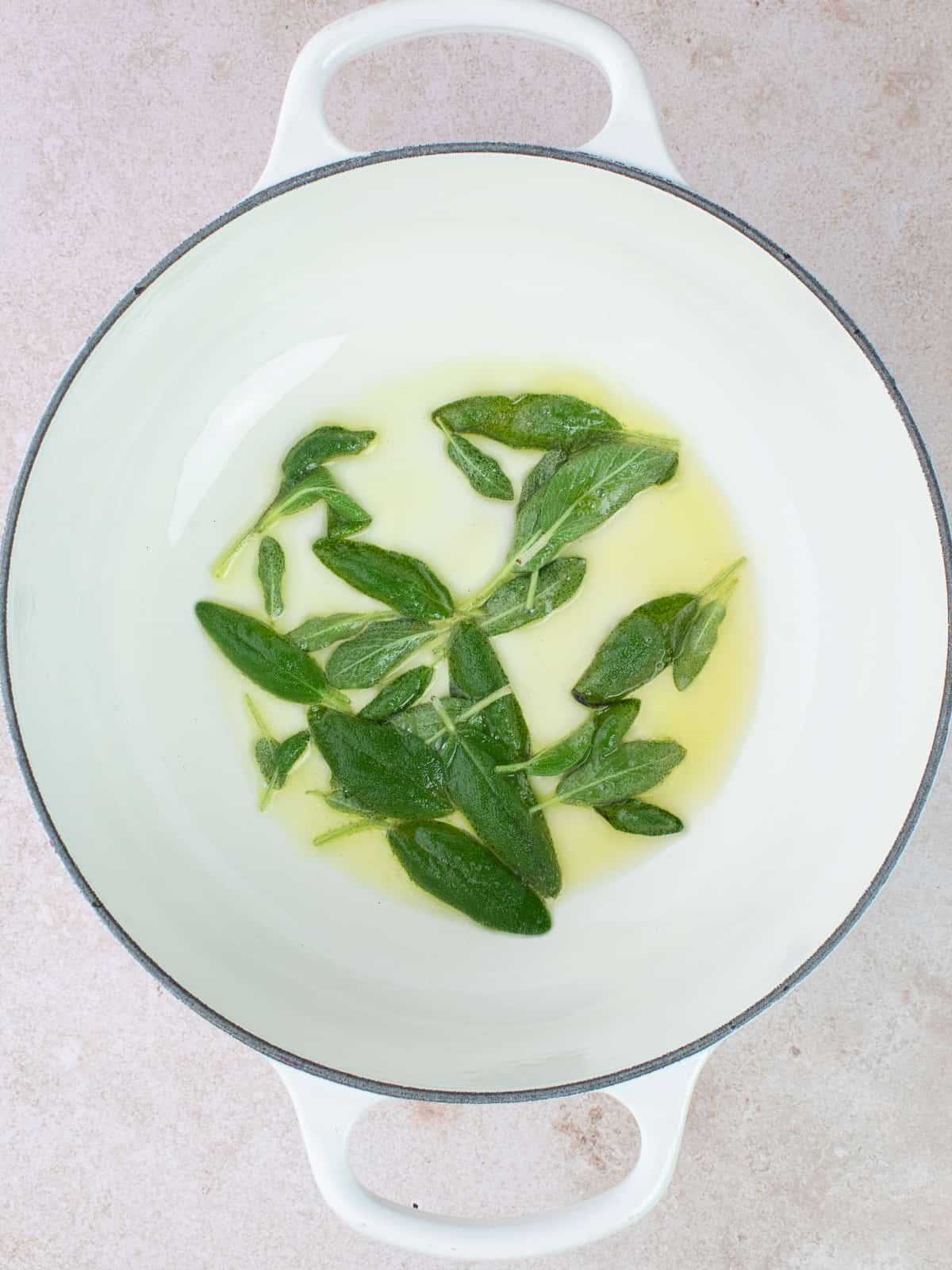 Olive oil and sage leaves are frying in a pot