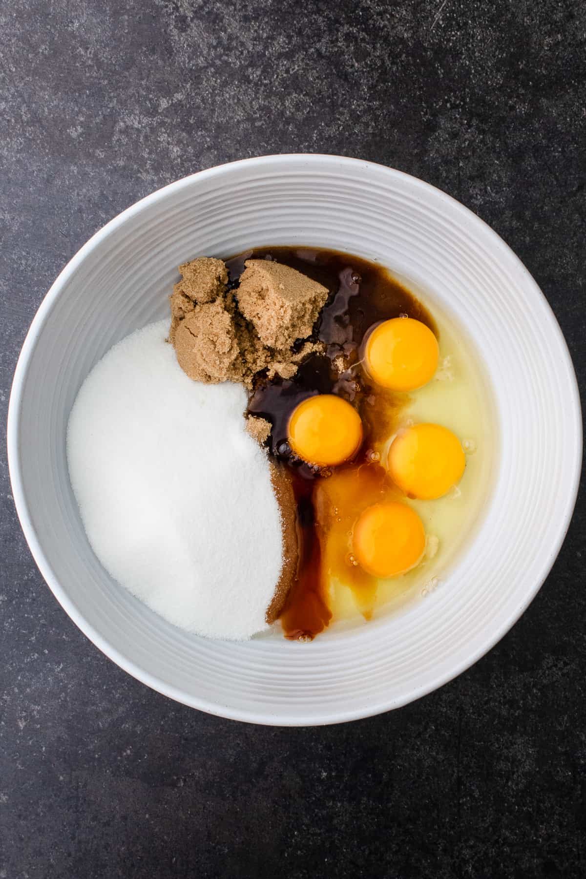 A bowl containing white sugar, brown sugar, eggs and vanilla