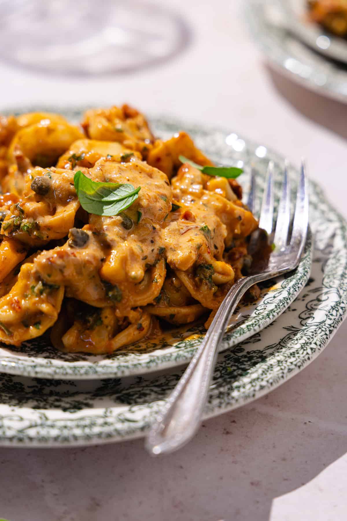 Sun-dried tomato pasta garnished with fresh basil served in a dish with a fork tucked next to the pasta.