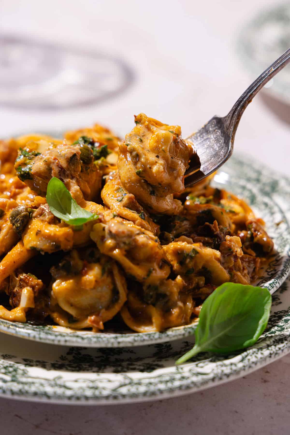 A fork digs into the sun-dried tomato pasta garnished with fresh basil in a dish.