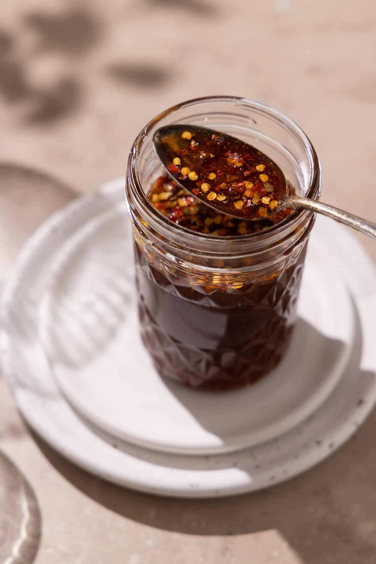 Hot honey is in a mason jar on top of 2 plates. A hand holds a spoon with hot honey.