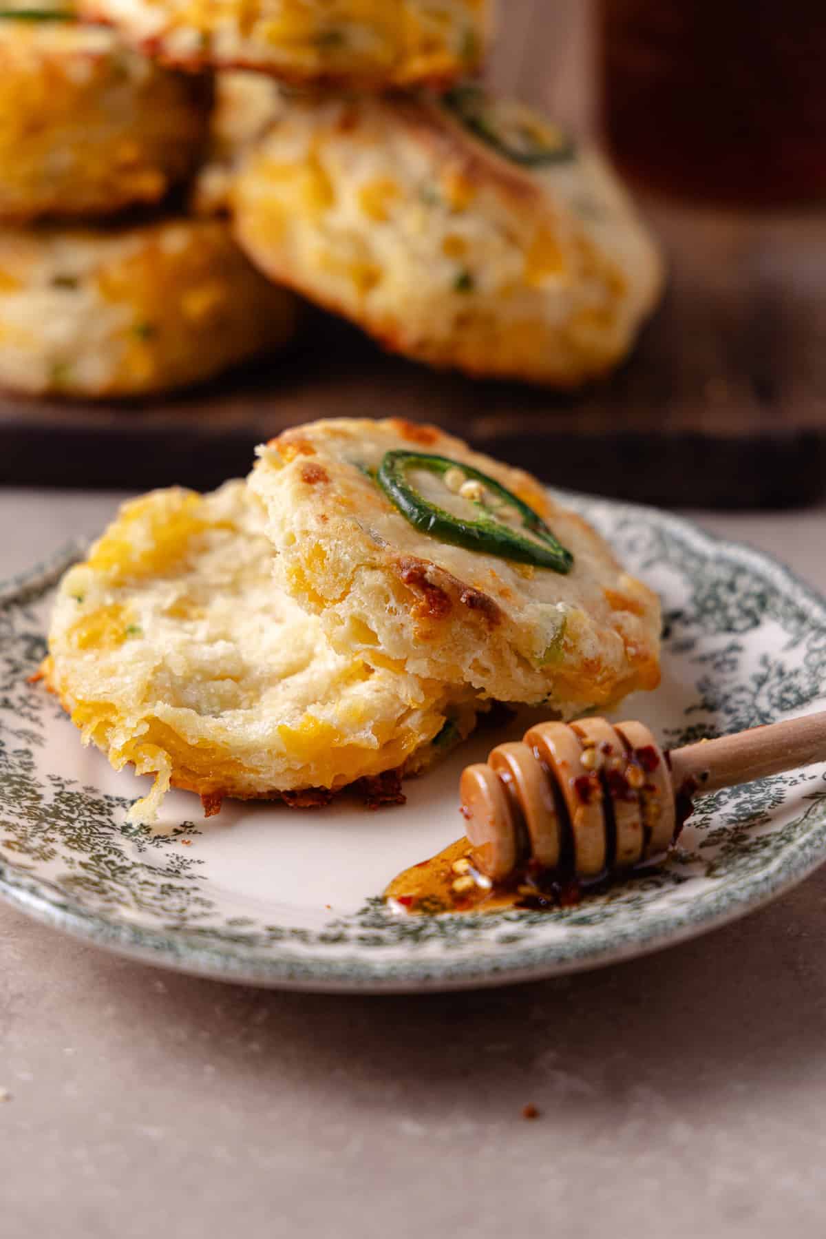 A biscuit split in half and placed on a small plate. A honey dipper with hot honey is also pooled on the plate.