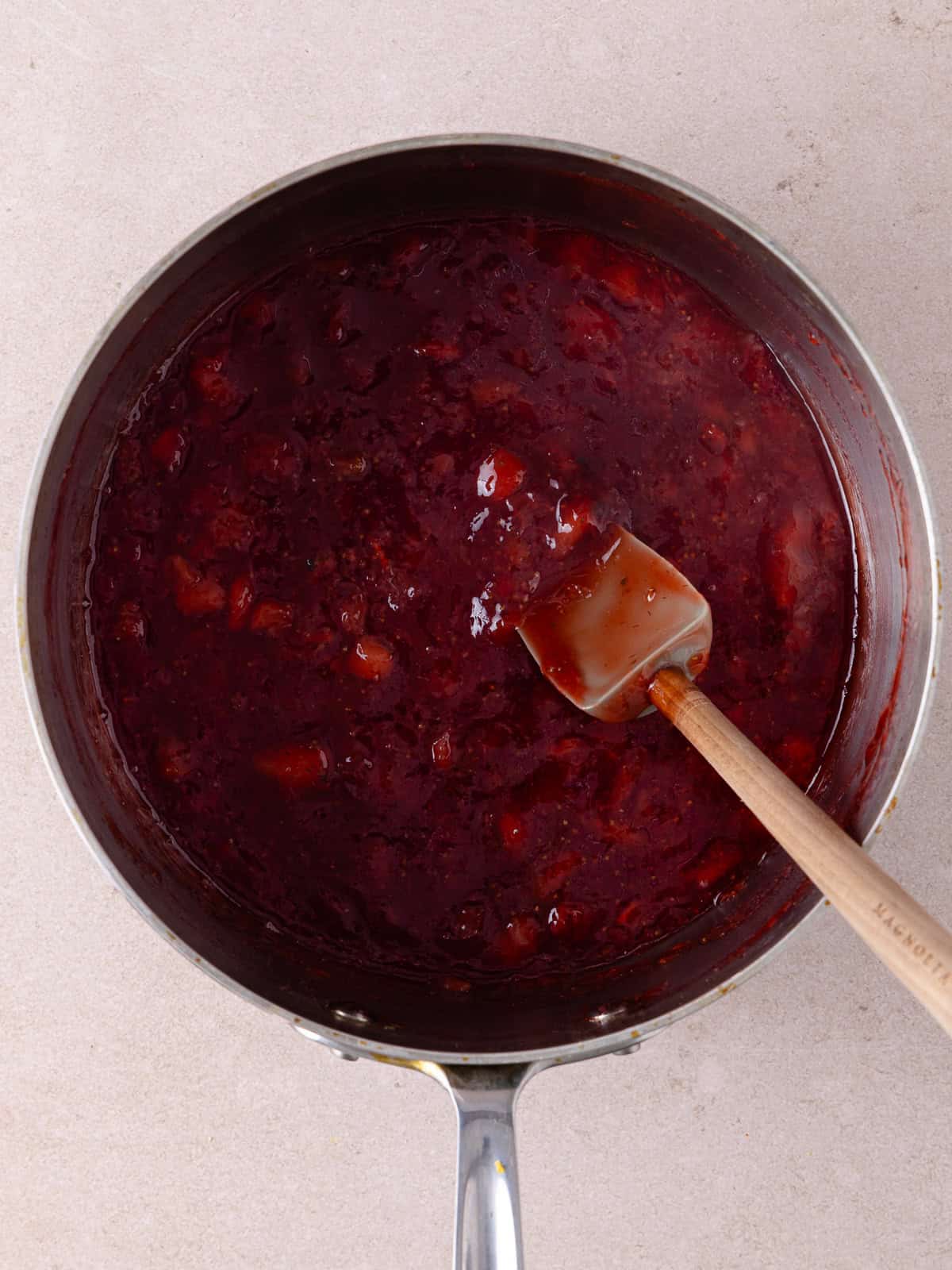 Homemade strawberry jam cooked in a small saucepan. Fresh strawberries have cooked down and the jam has thickened up.