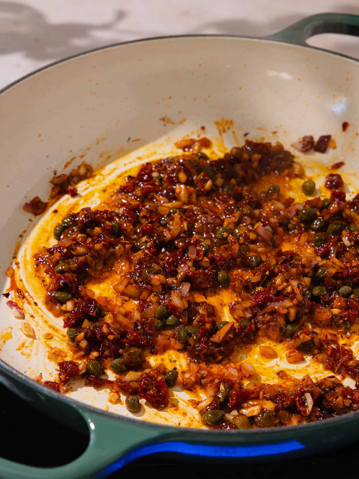 Sun-dried tomato oil, sun-dried tomatoes, capers, onion, garlic, gochujang, Italian seasoning, red pepper flakes and smoked paprika are sauteed a large pan.