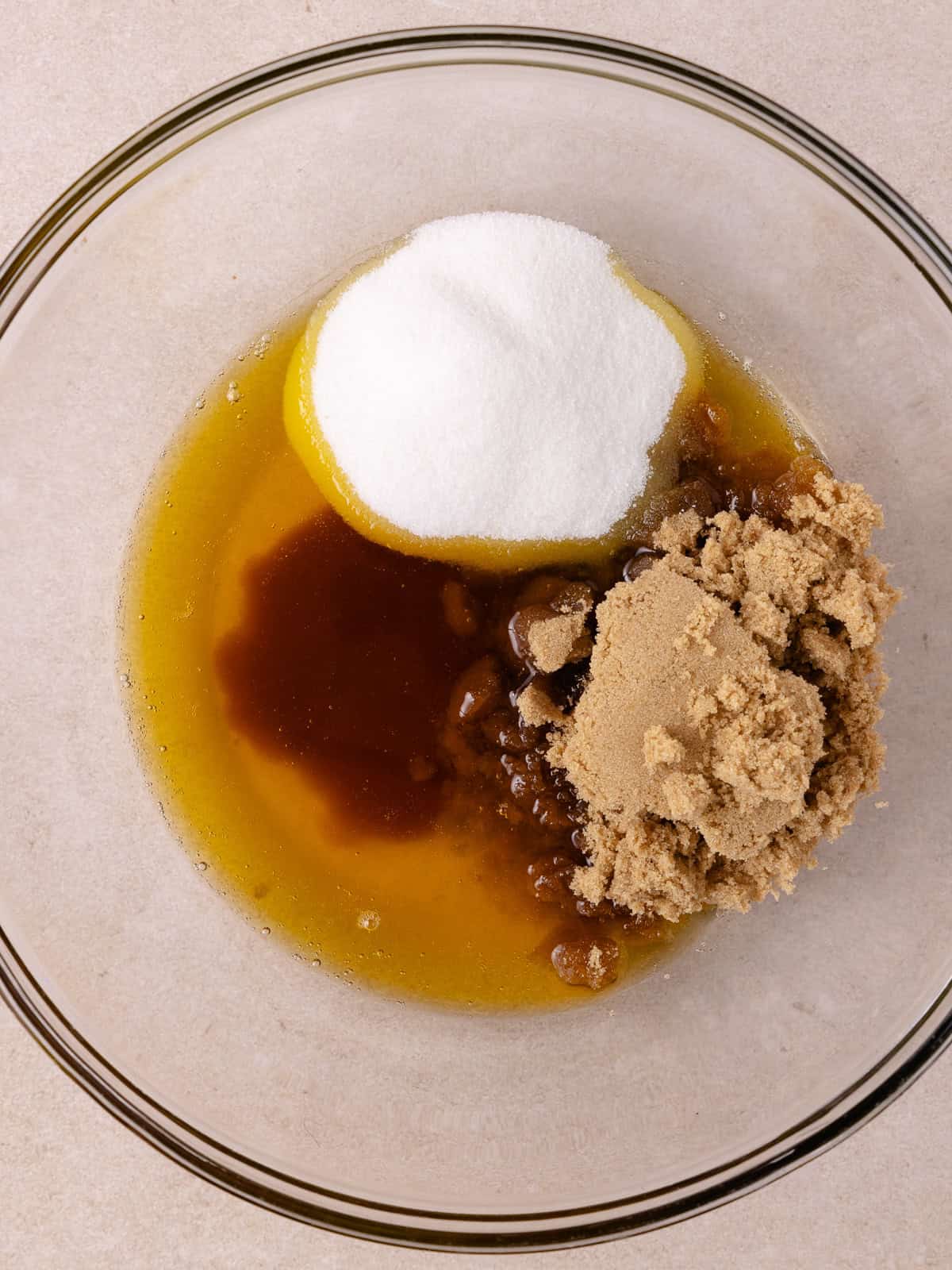 Brown butter, brown sugar and white sugar is added to a large glass bowl.