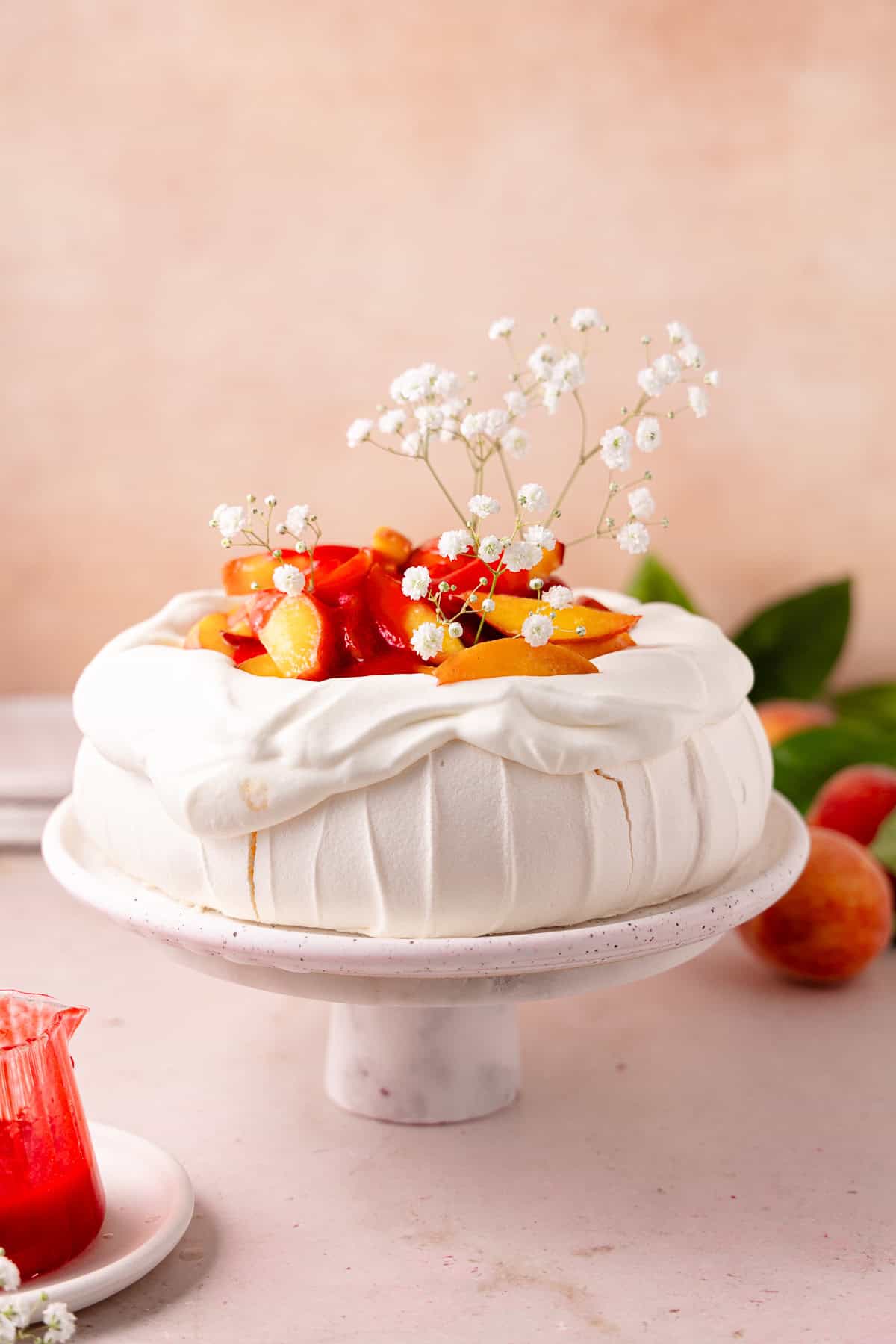 Peach melba pavlova topped with whipped cream, peaches and raspberry sauce sitting on a cake stand.