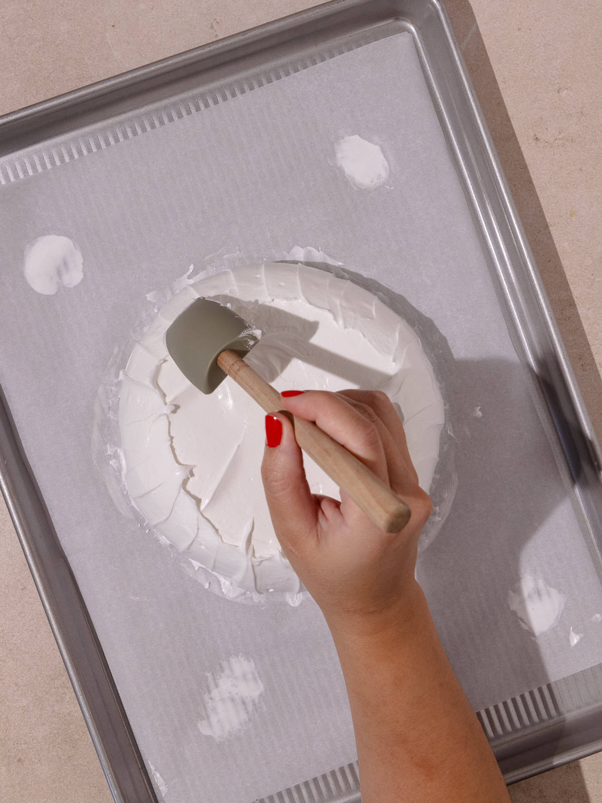 A hand shapes the pavlova with a small spatula.