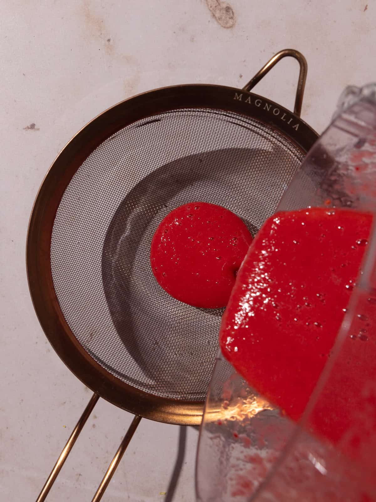 Raspberry coulis is being strained into a small glass bowl.