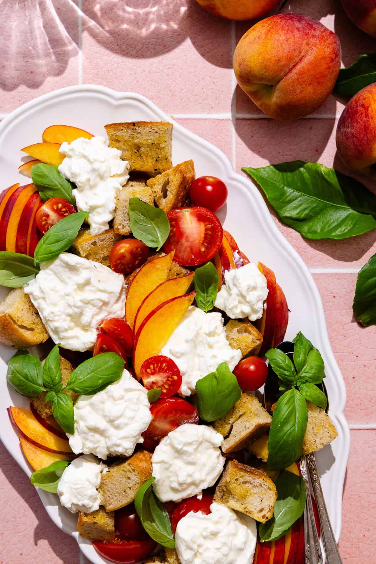 A platter with peach panzanella salad, featuring sliced peaches, cherry tomatoes, homemade croutons, fresh basil and fresh burrata cheese.