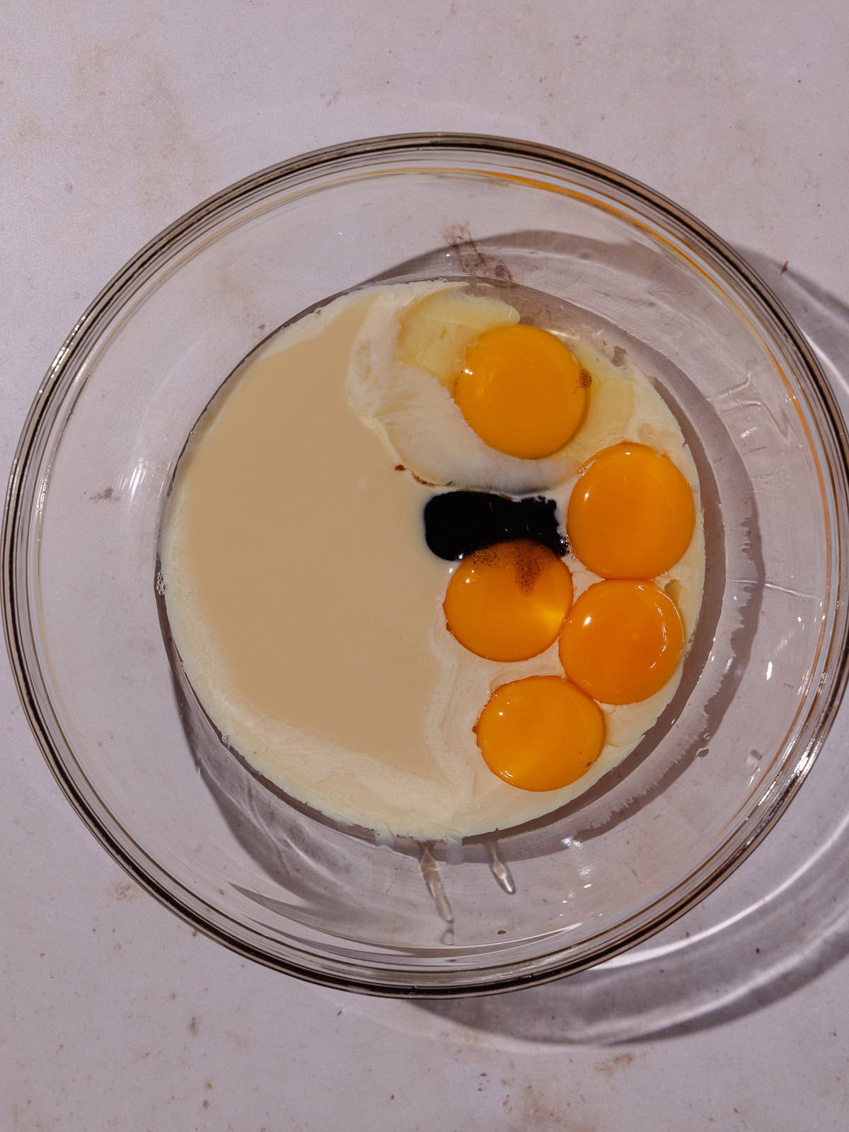 Egg, yolks, sweetened condensed milk and vanilla are added to a glass bowl.