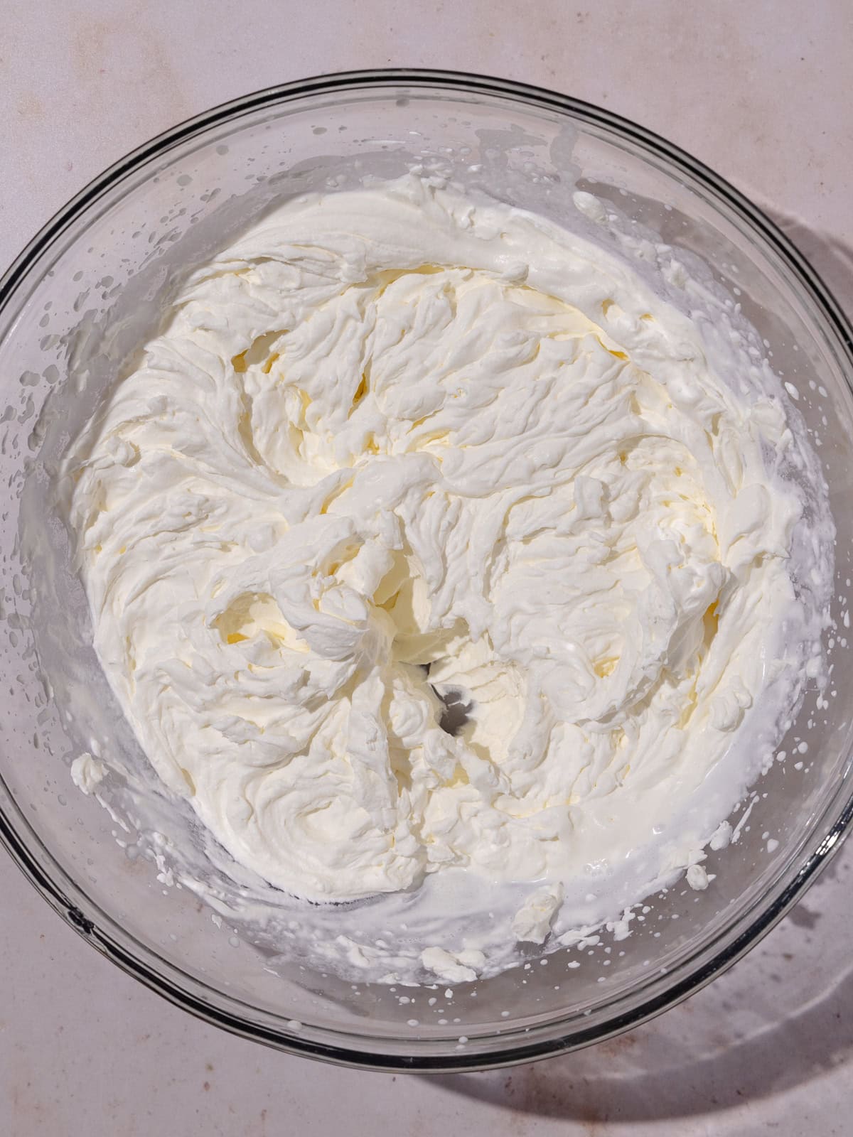 Heavy cream is whipped to stiff peaks in a large bowl.