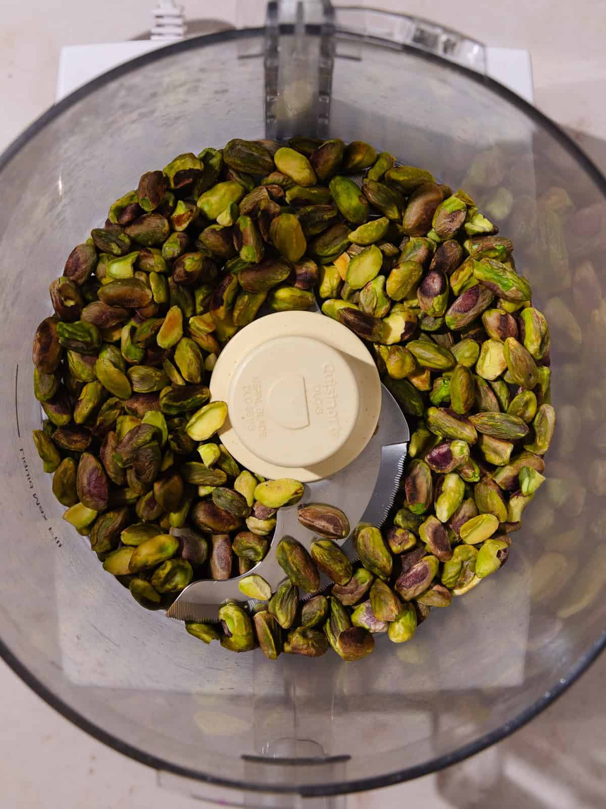 Toasted pistachios are added to the bowl of a food processor.