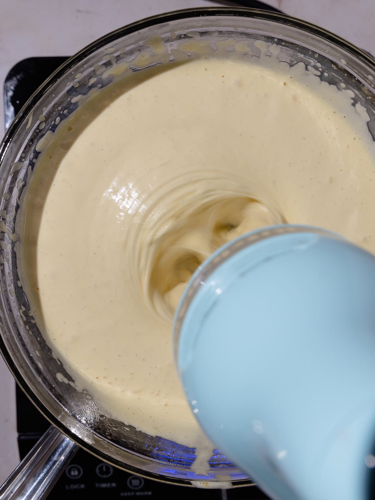 Yolk/condensed milk mixture sits over a pot of simmering water, while being whipped with a hand-held mixture.