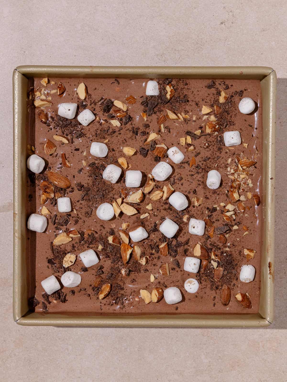 Rocky road ice cream is transferred to a container. Ice cream is also topped with marshmallows, chopped almonds and finely chopped chocolate.