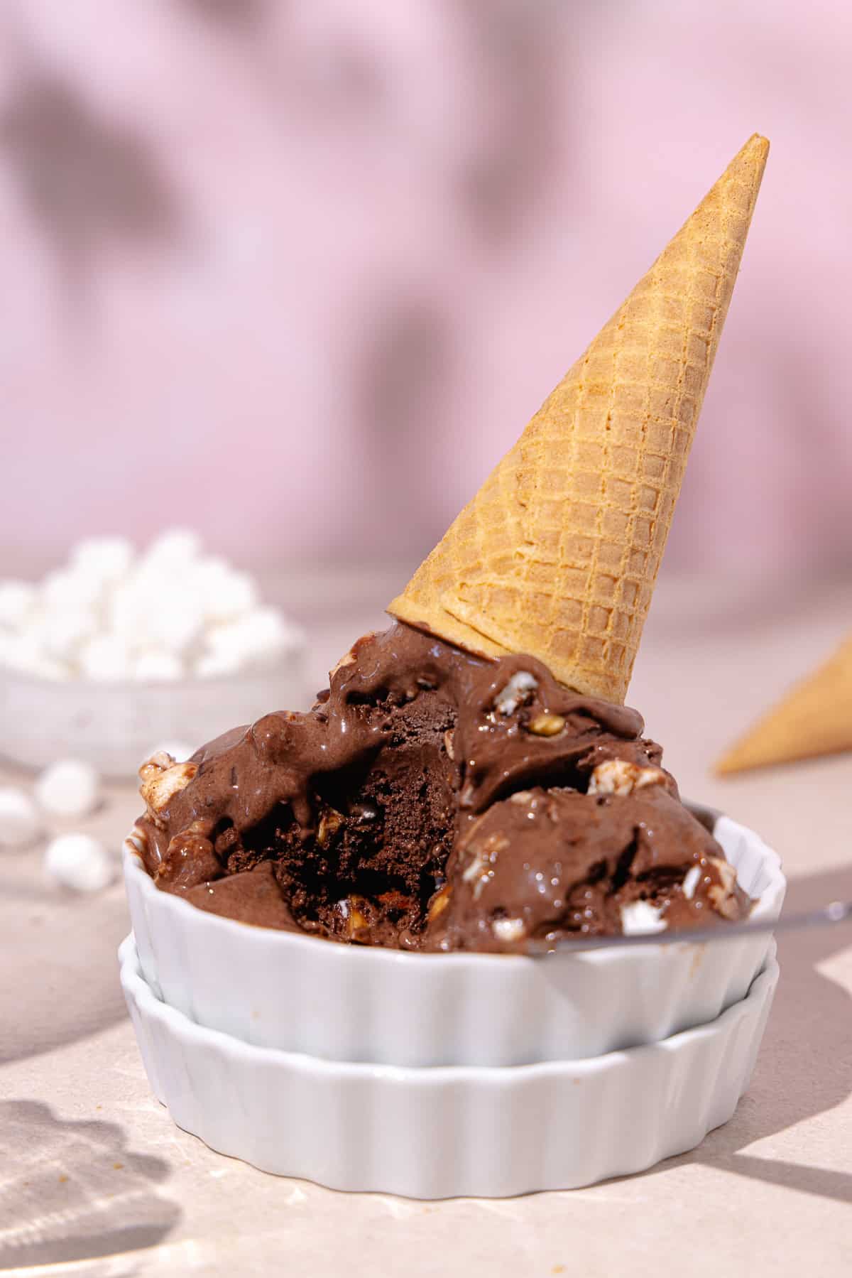 Rocky road ice cream in a bowl with sugar cone and spoon.