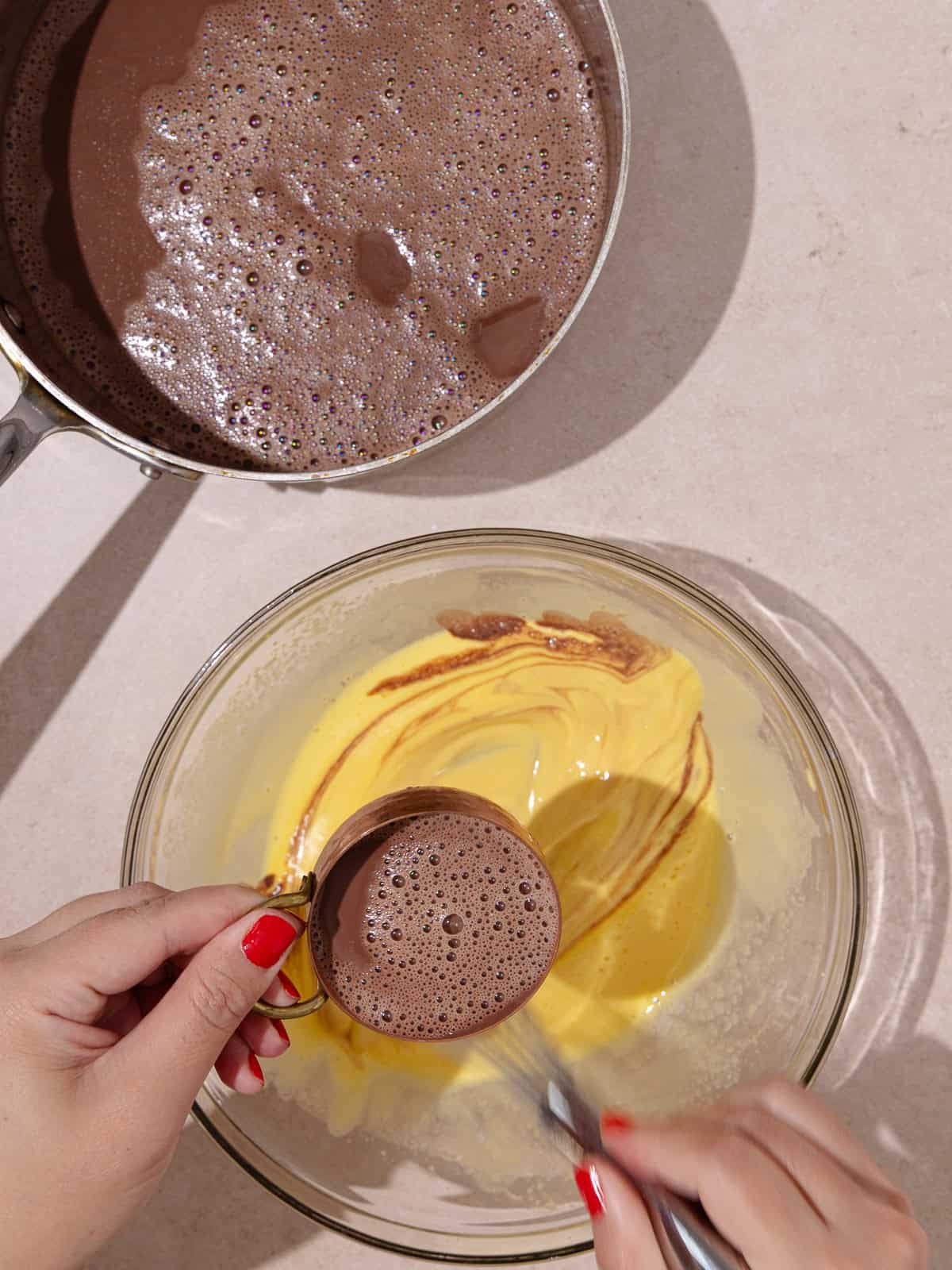 Warm cream/milk mixture is slowly being added and whisked to the yolk mixture.