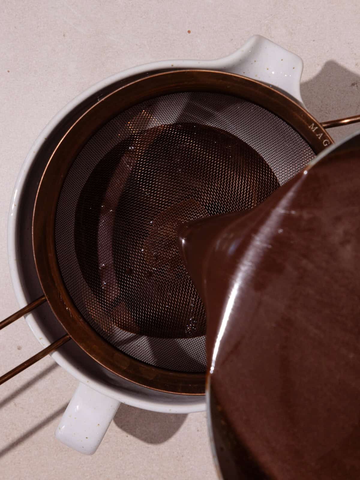 Chocolate custard is strained into a spouted bowl.