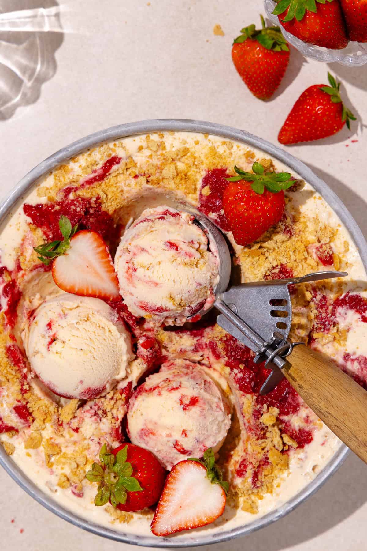 Scoops of Strawberry cheesecake ice cream in a round cake pan with fresh strawberries all around.