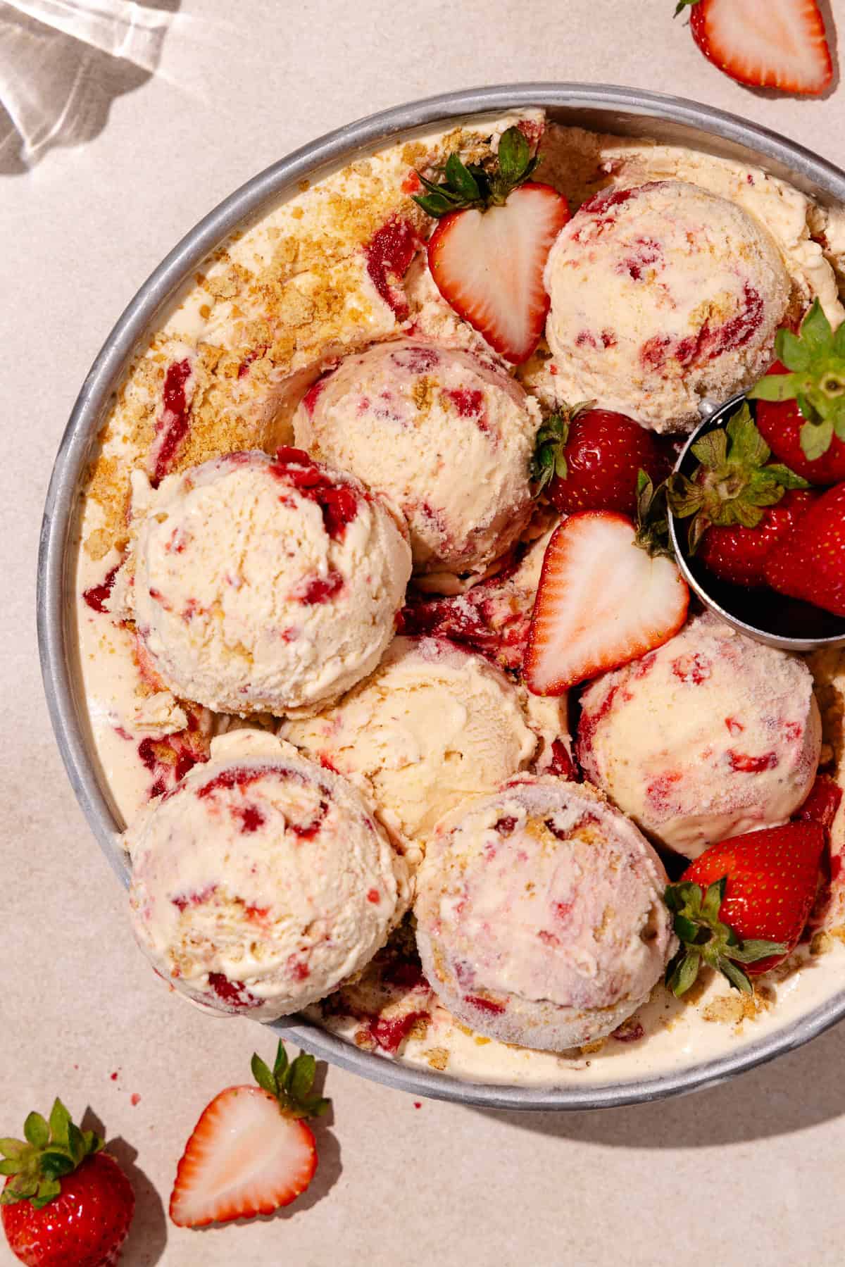 Scoops of Strawberry cheesecake ice cream in a round cake pan with fresh strawberries all around.