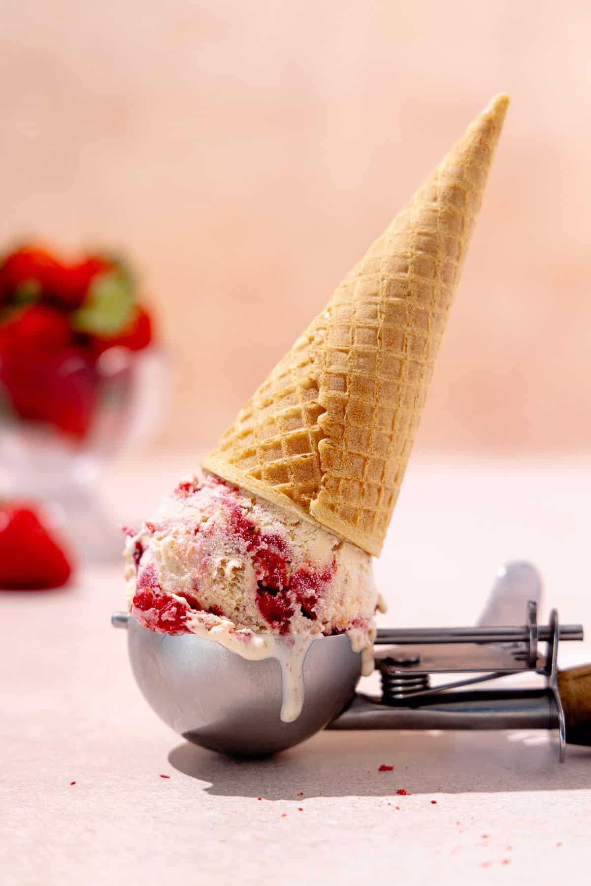 Ice cream scoop with strawberry cheesecake ice cream topped with ice cream cone.