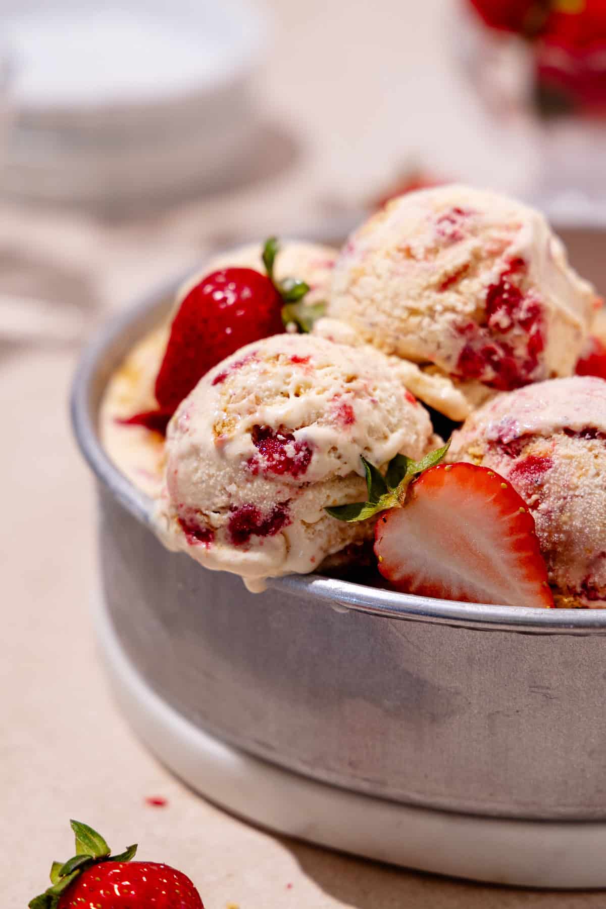 Close up of scoops of Strawberry cheesecake ice cream in a round cake pan with fresh strawberries all around.