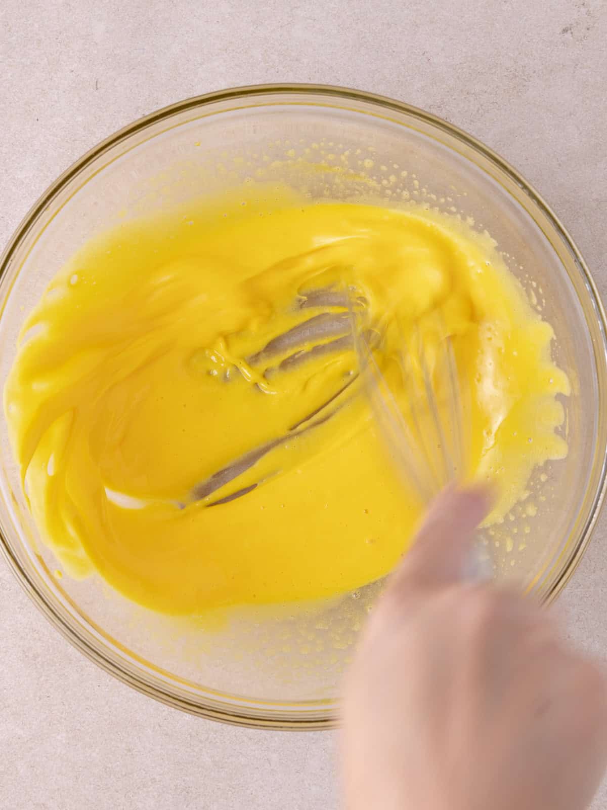 Egg yolks and sugar are whipped in a medium sized glass bowl.