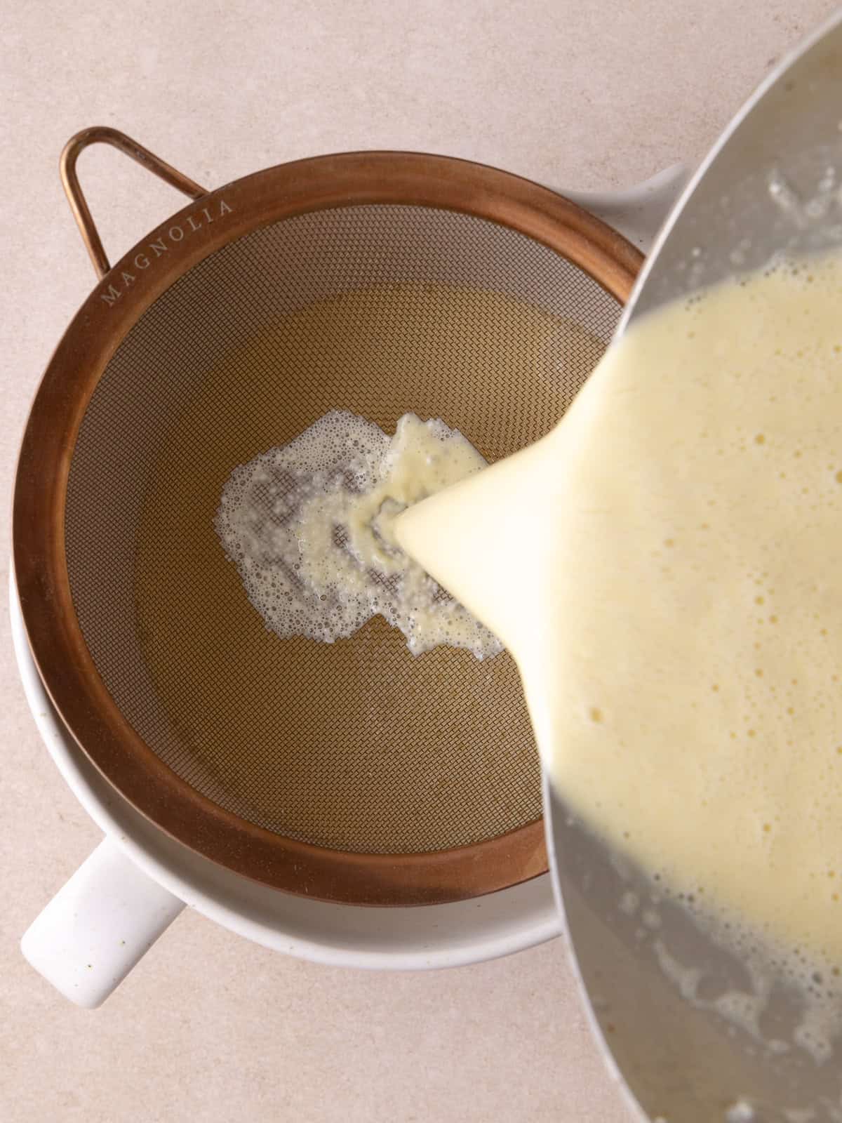 Custard is poured through a fine sieve sitting over a bowl.