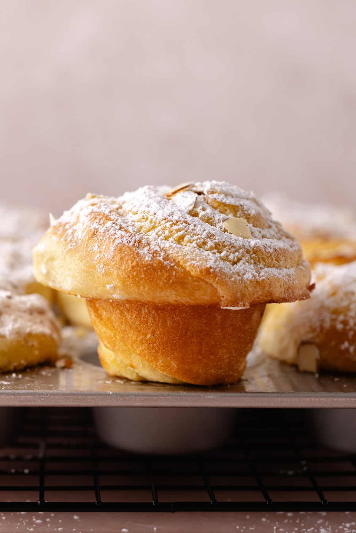 Almond croissant rolls sits on the edge of a muffin pan.