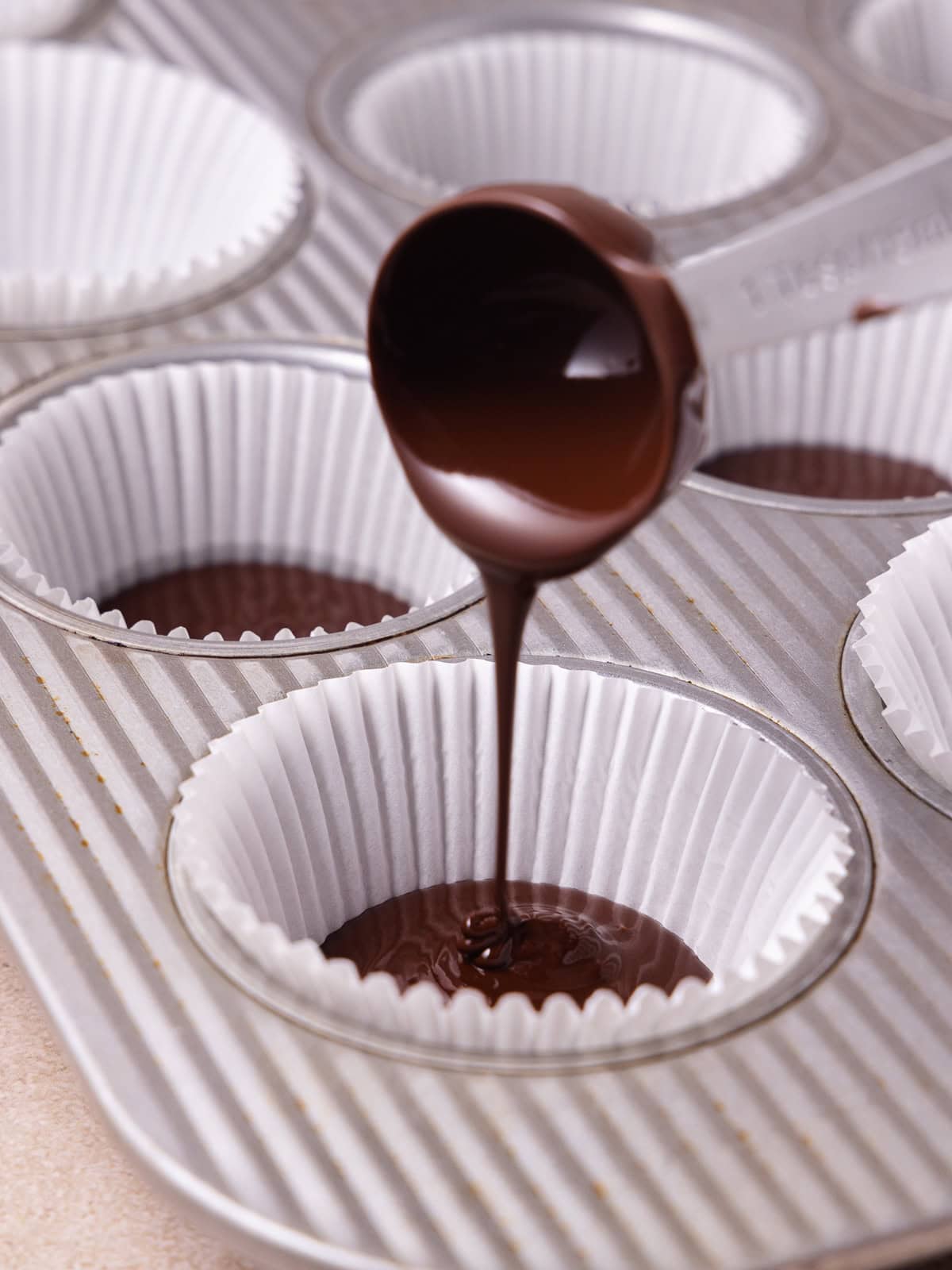 A tablespoon of melted chocolate is poured into the bottom of a cupcake liner.