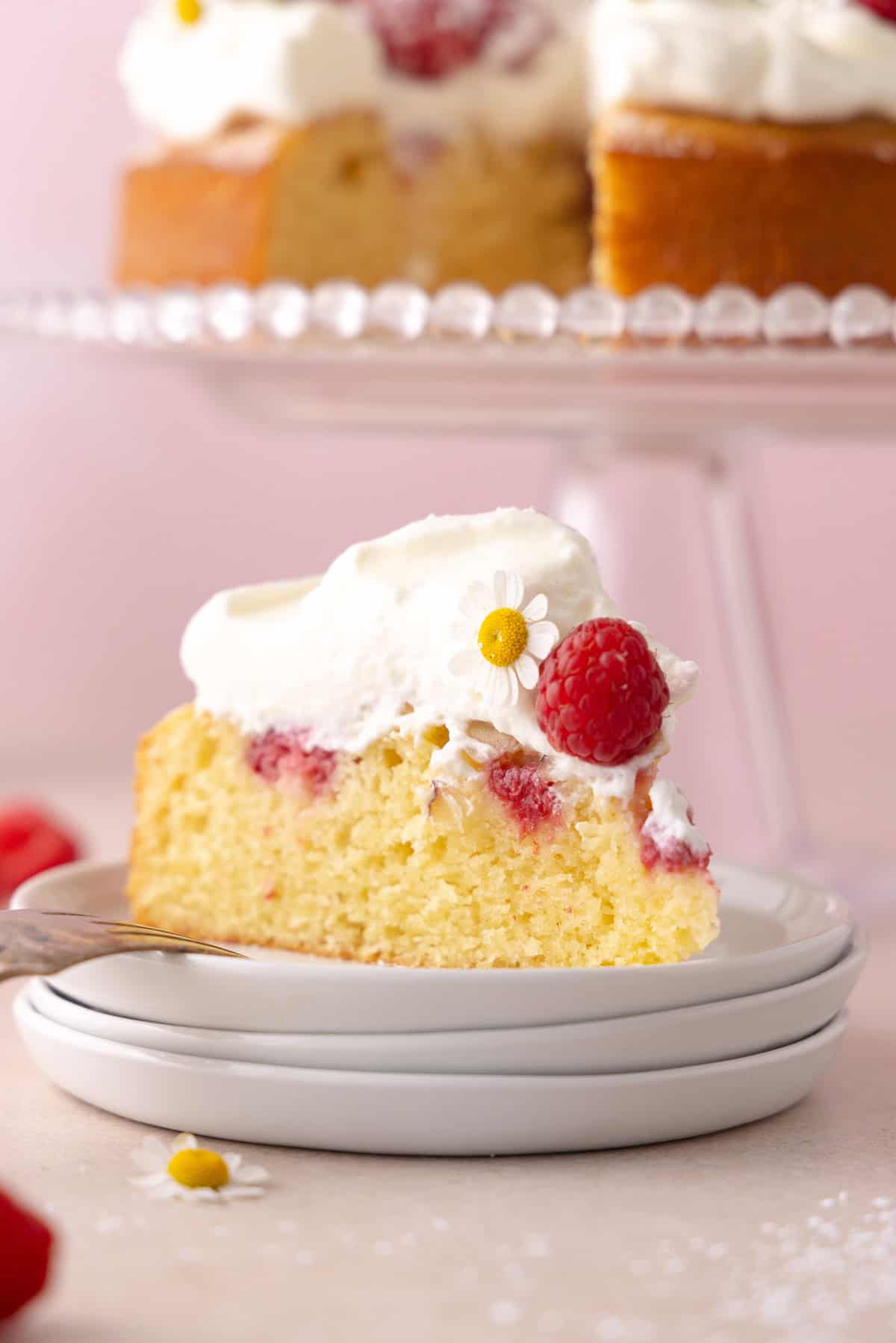 A slice of raspberry olive oil cake is on a stack of white plates.