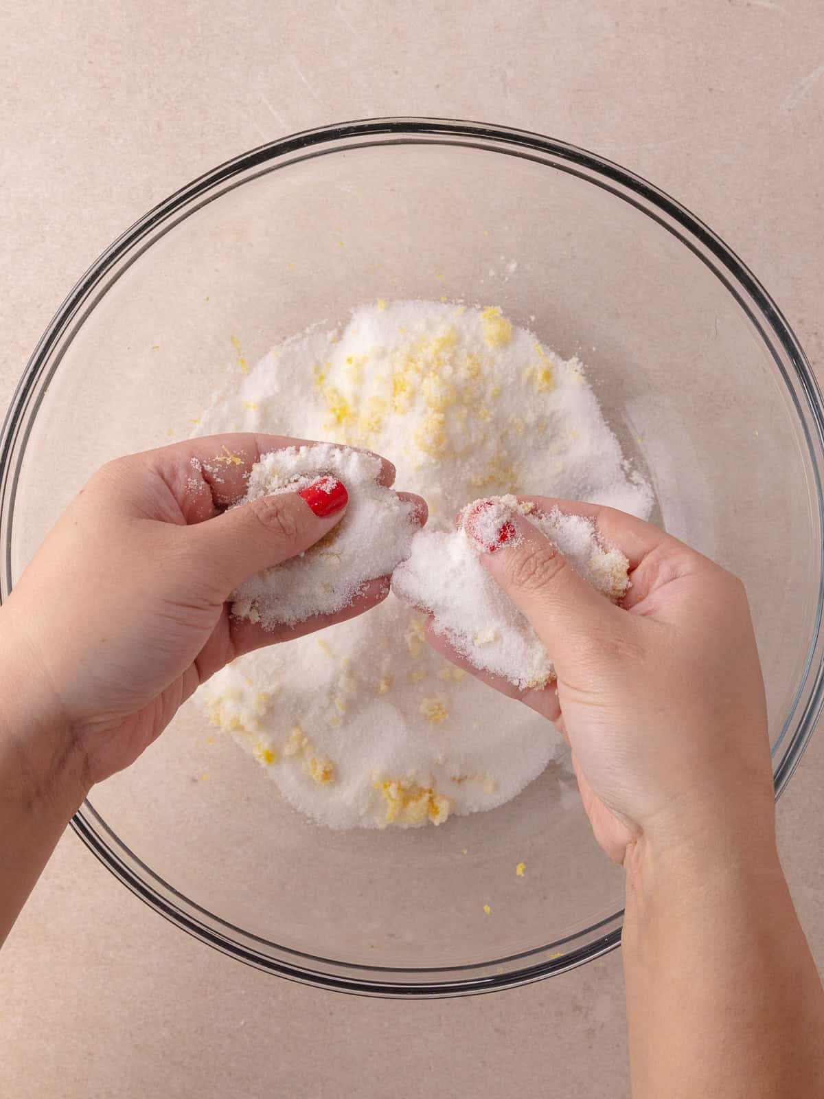 White sugar and fine lemon zest is combined and rubbed together in a large mixing bowl.