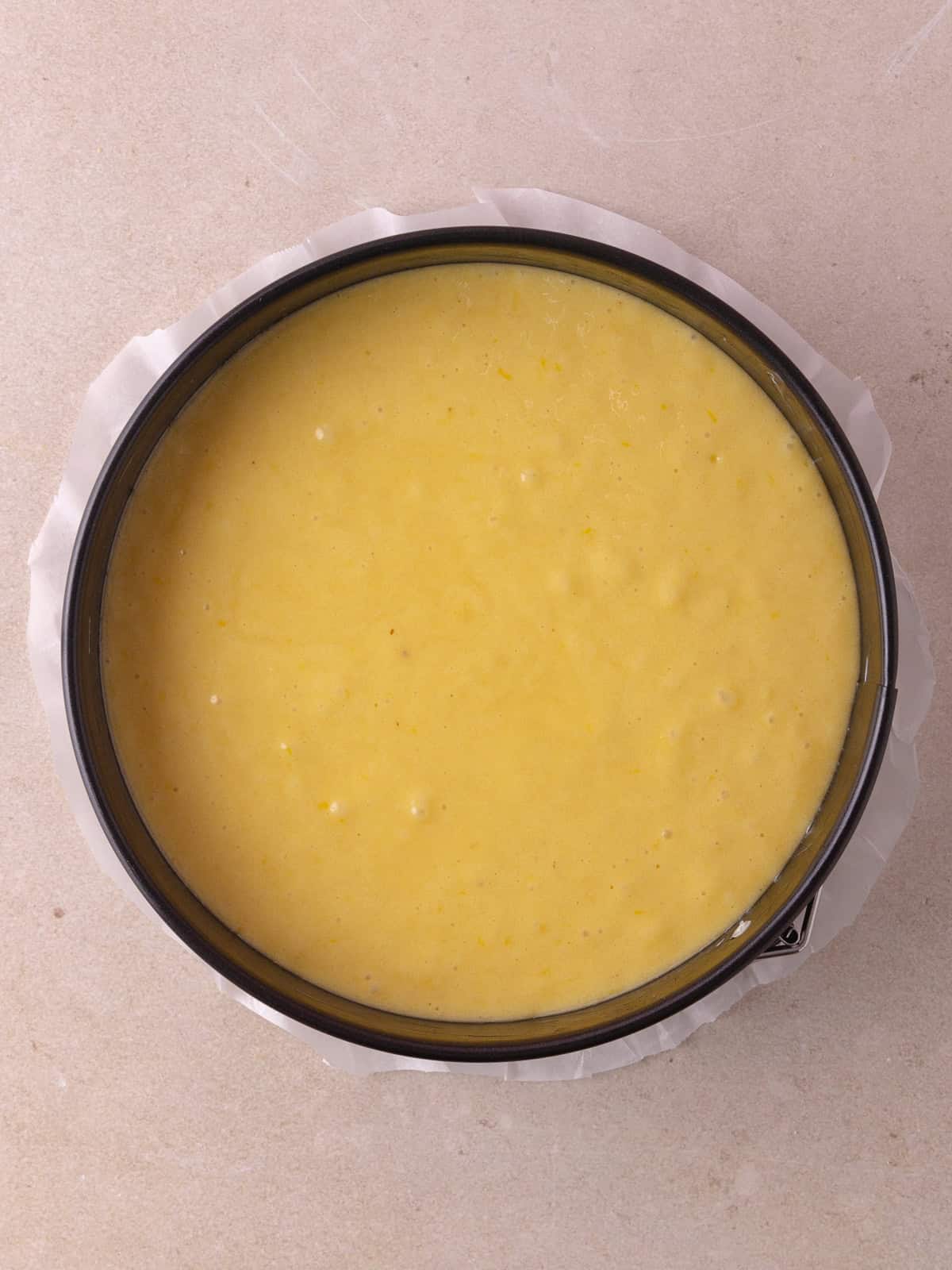 Cake batter is poured into a parchment paper-lined 8-inch round springform pan.