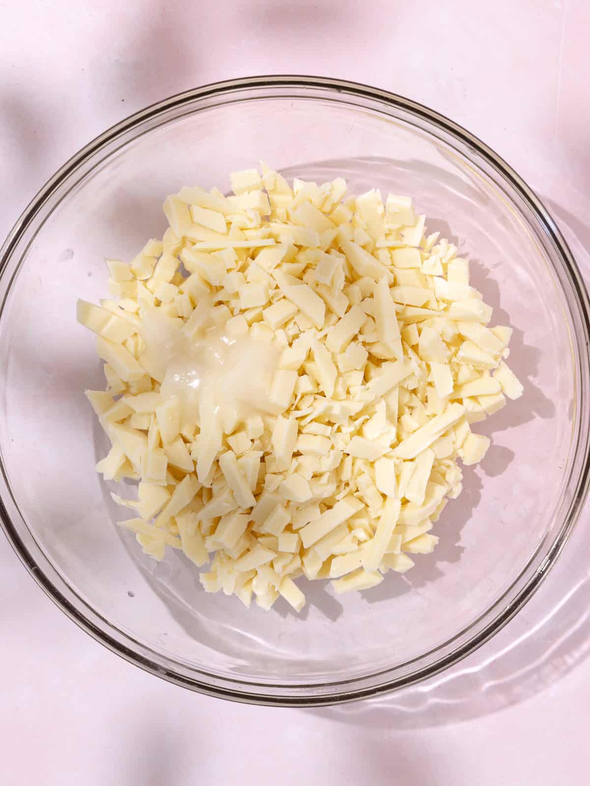 Chopped white chocolate and coconut oil is in a medium glass bowl.