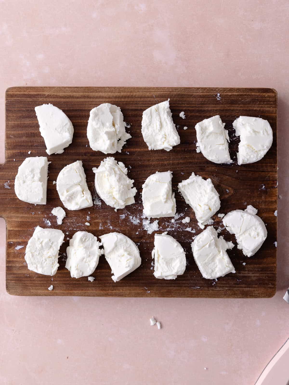 Goat cheese log is cut into 16 pieces on a wooden cutting board.