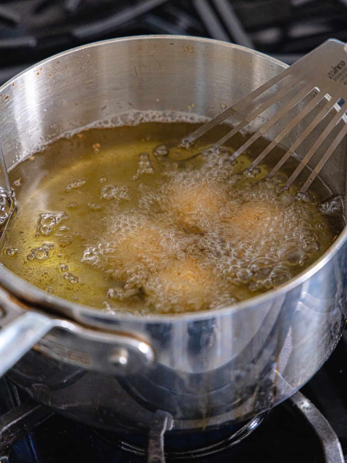 Goat cheese balls are deep fried in a small saucepan.