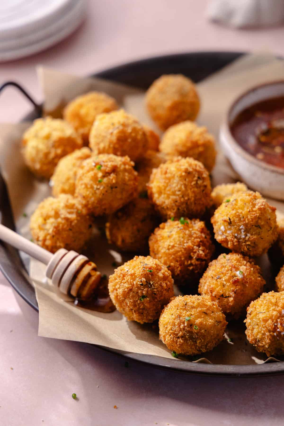 Fried goat cheese balls on a serving platter with a bowl of hot honey.