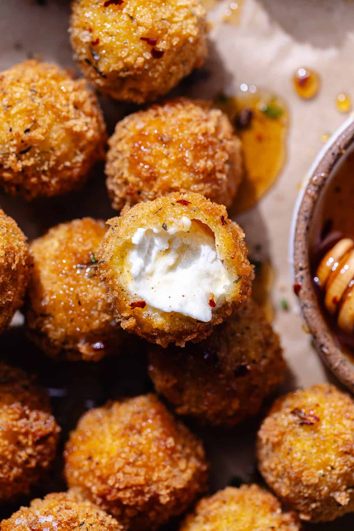 Close up of fried goat cheese balls on a serving platter with a bowl of hot honey.