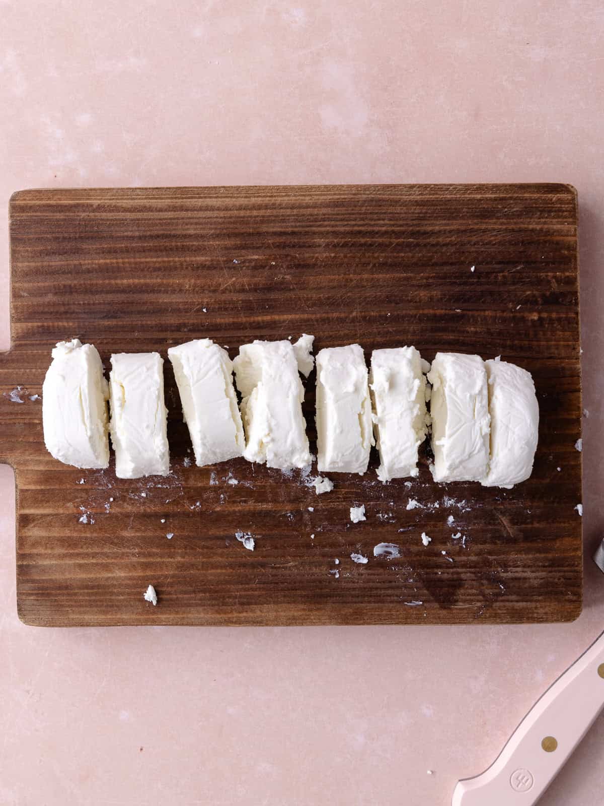 Goat cheese log is cut into 8 pieces on a wooden cutting board.