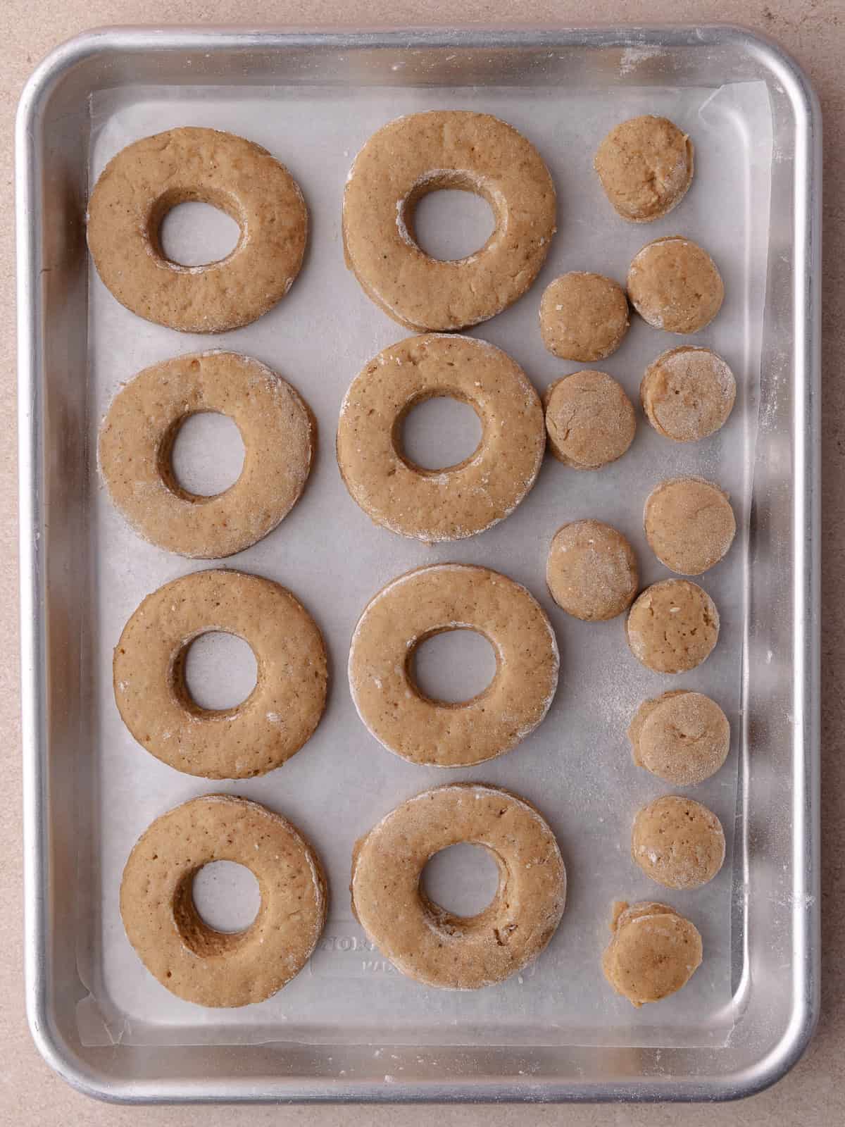 Eight round donuts and 11 donut holes are cut and placed on a small baking sheet.