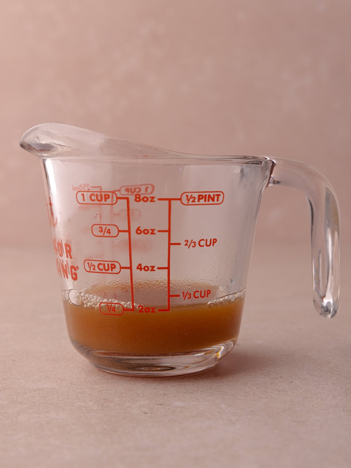 Apple cider is cooked and reduced down to a fourth of a cup and is pour into a glass measuring cup.