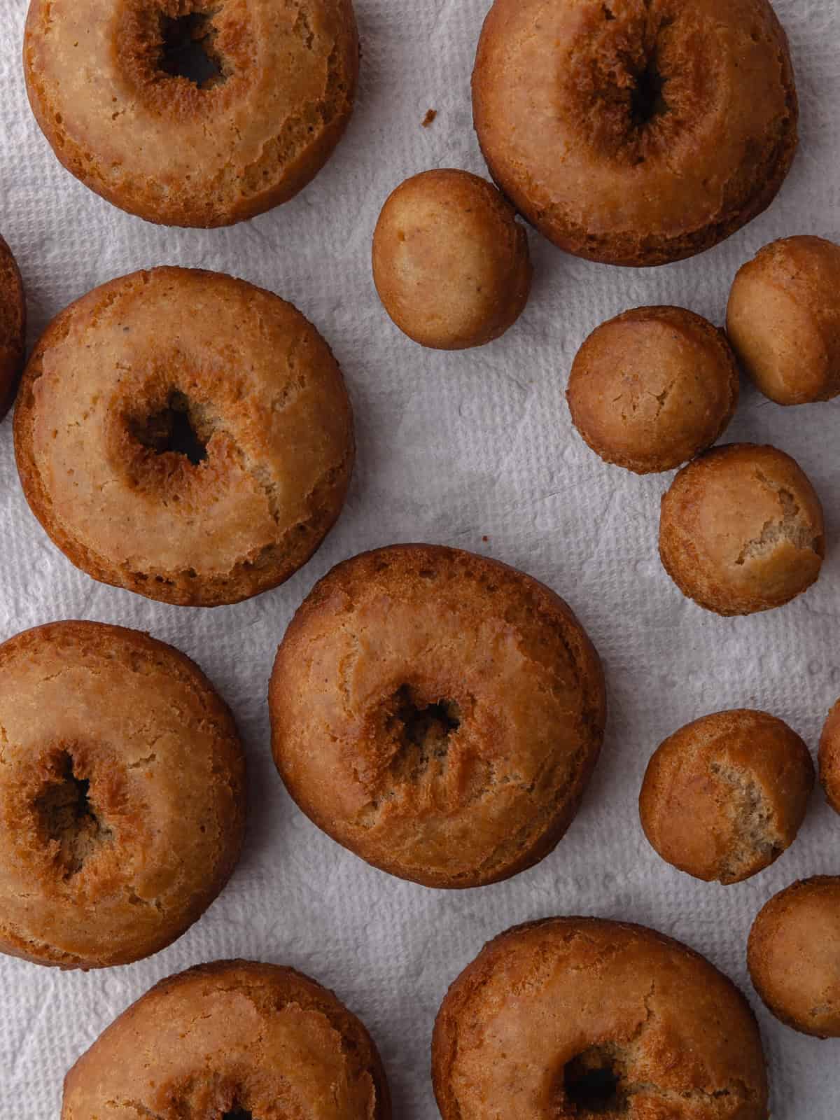 Golden brown fried donuts and donut holes are on a wire rack lined with paper towels.