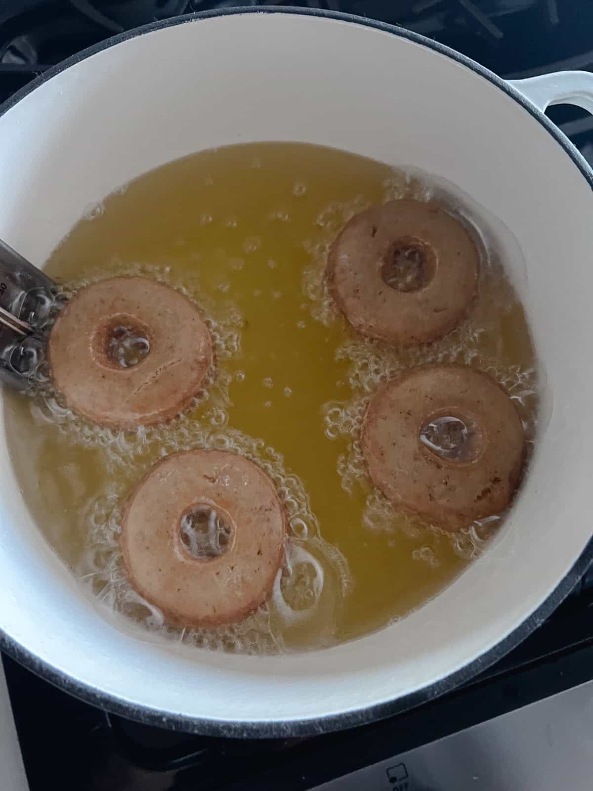 Four mini apple cider donuts are fried in a large dutch oven with a candy thermometer hooked to the side of the pot.