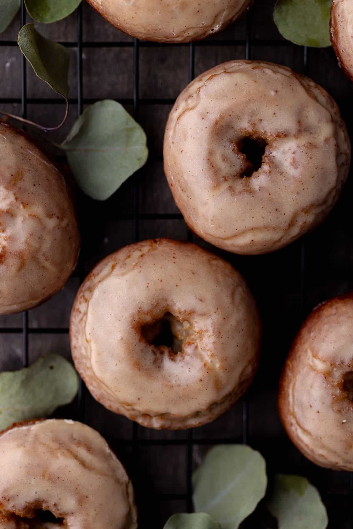 Fried and glazed apple cider donuts are on a wire rack surrounded by dried leaves.