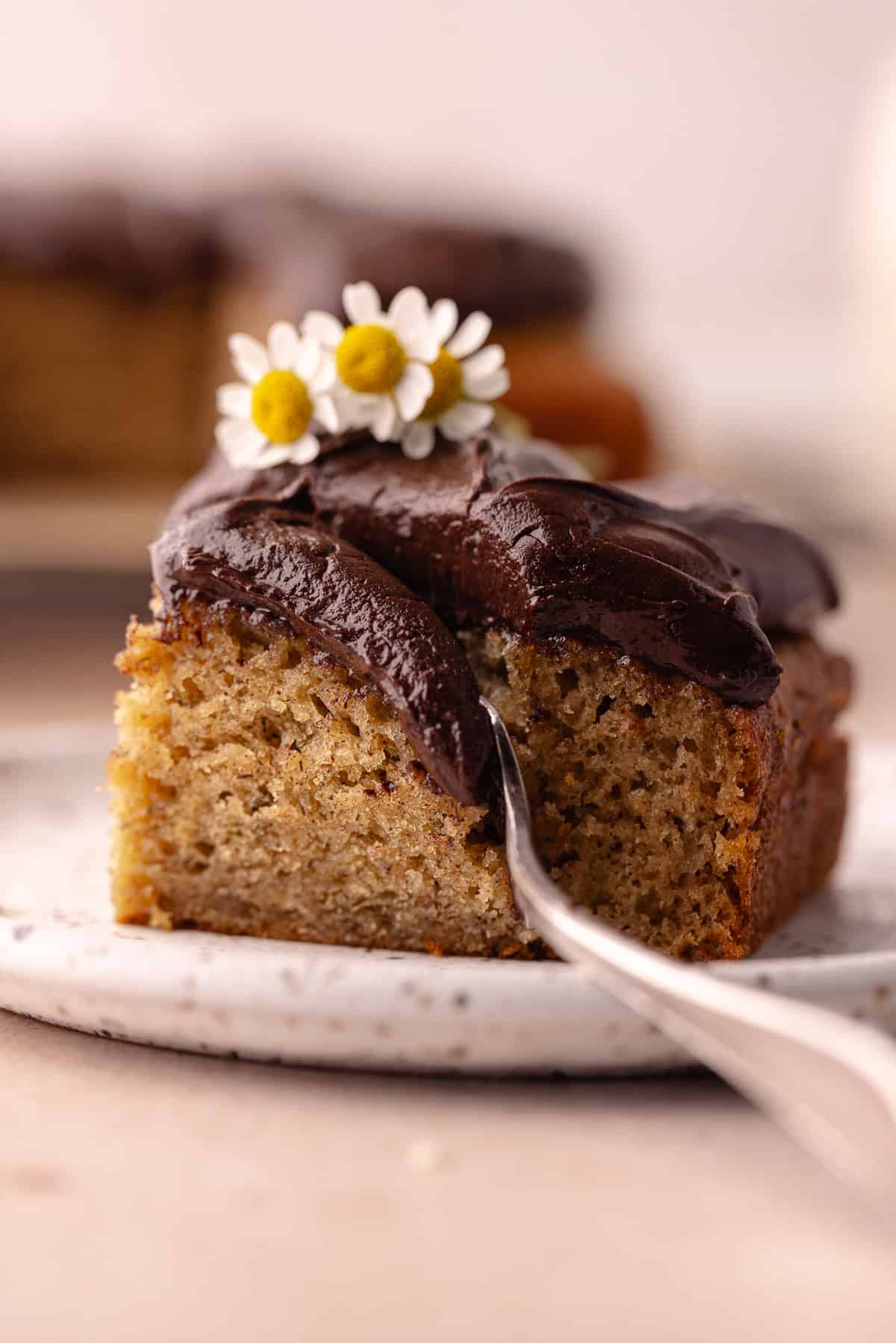 A slice of banana cake with chocolate frosting on a small plate