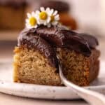 A slice of banana cake with chocolate frosting on a small plate. Feature photo.