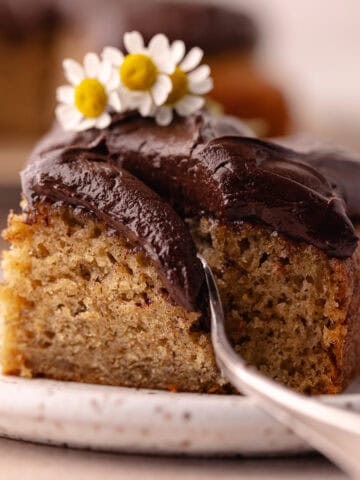 A slice of banana cake with chocolate frosting on a small plate. Feature photo.