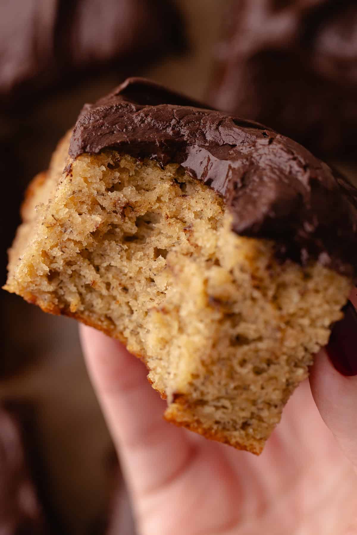 A hand holds a slice of banana cake with a bite taken out.